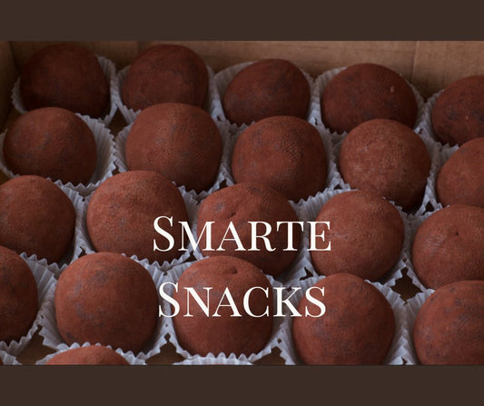 Handgemachte rohe Kakaotrüffel in Papierförmchen, ordentlich angeordnet in einer Schachtel, mit dem Text „Smarte Snacks“ darüber.