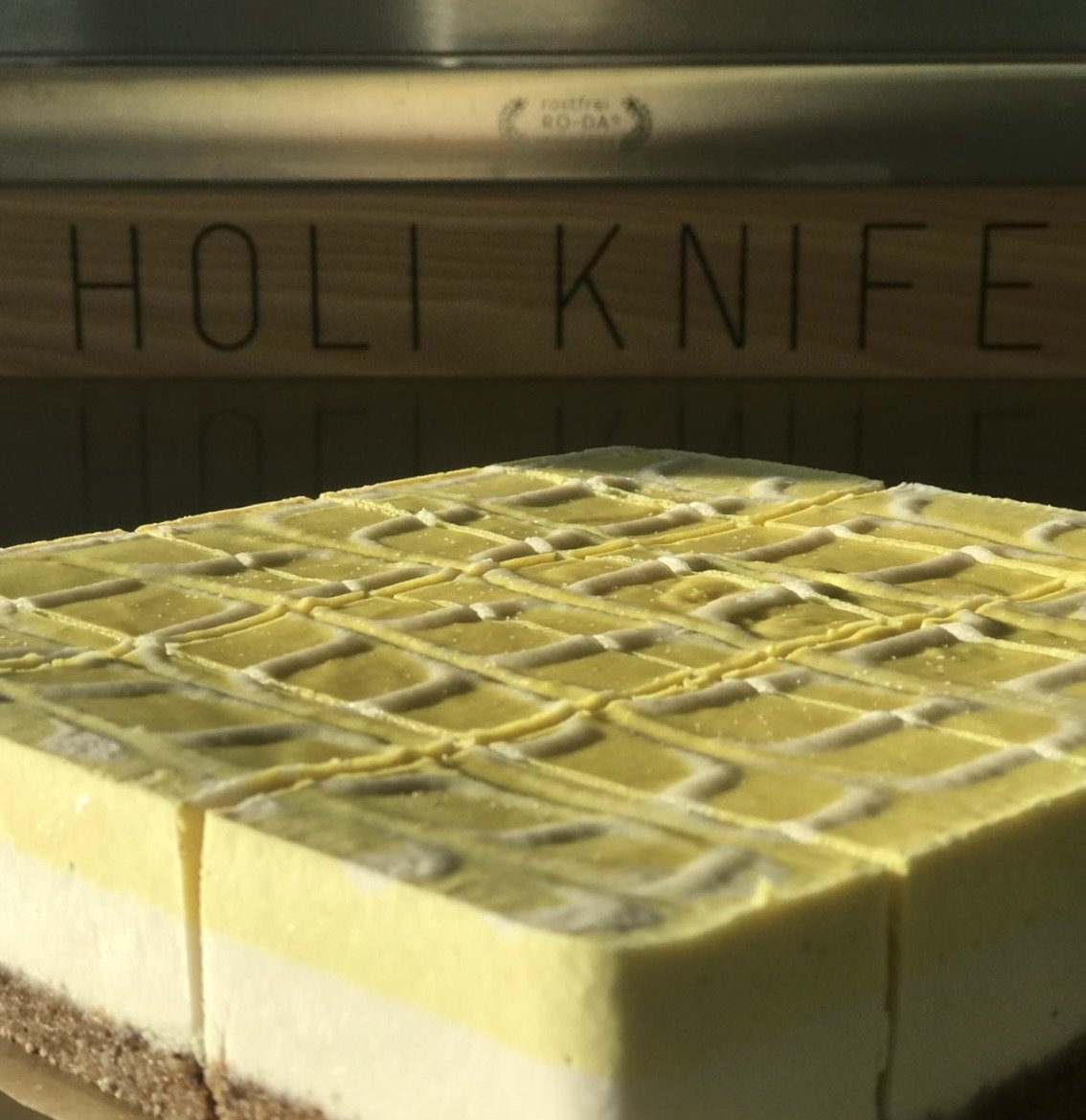 Zitronen-Rohkostkuchen ohne Zucker mit Cashewcreme auf Nussboden, vegan und glutenfrei, aufgenommen im Sonnenlicht bei Holi Sweets in München.